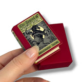 A hand holds a miniature red book-shaped box labeled 'The Legend of Sissy Hallow' and 'Washington Irving' against a clean white background, with a matching red box behind it.