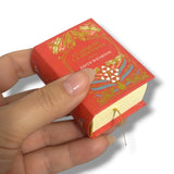 Hand holding a miniature red book with gold and blue designs on a white background La Edad de la Inocencia