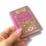 Hand holding a miniature book titled 'Sentido y Sensibilidad' by Jane Austen on a white background