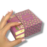 Hand opening a purple book-shaped gift box with gold text and patterns.Sentido y Sensibilidad