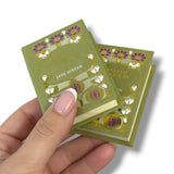 Hand holding a miniature book with decorative cover design on a white background. Orgullo y Prejuicio