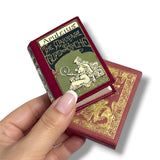 Miniature book titled 'The Marriage of Cupid and Psyche' held by a hand on a white background