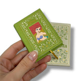 Hand holding a miniature book with a Disney character on the cover against a white background. La Sirenita