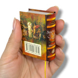 Hand holding a miniature book with colorful cover and visible text Sueño de una noche de Verano William Shakespeare