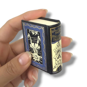 Hand holding a miniature book with decorative cover against a white background. Gulliver's Travels