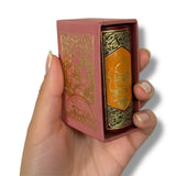 Hand holding a small, ornately designed box with gold and pink colors on a white background