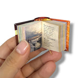 Miniature book held open by a hand with visible text and image on a white background