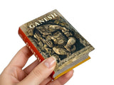 Miniature book with 'Ganesh' on the cover held by a hand against a white background