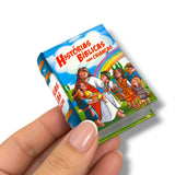 A hand holding a miniature hardcover book titled 'Histórias Bíblicas Para Crianças' against a plain white background.